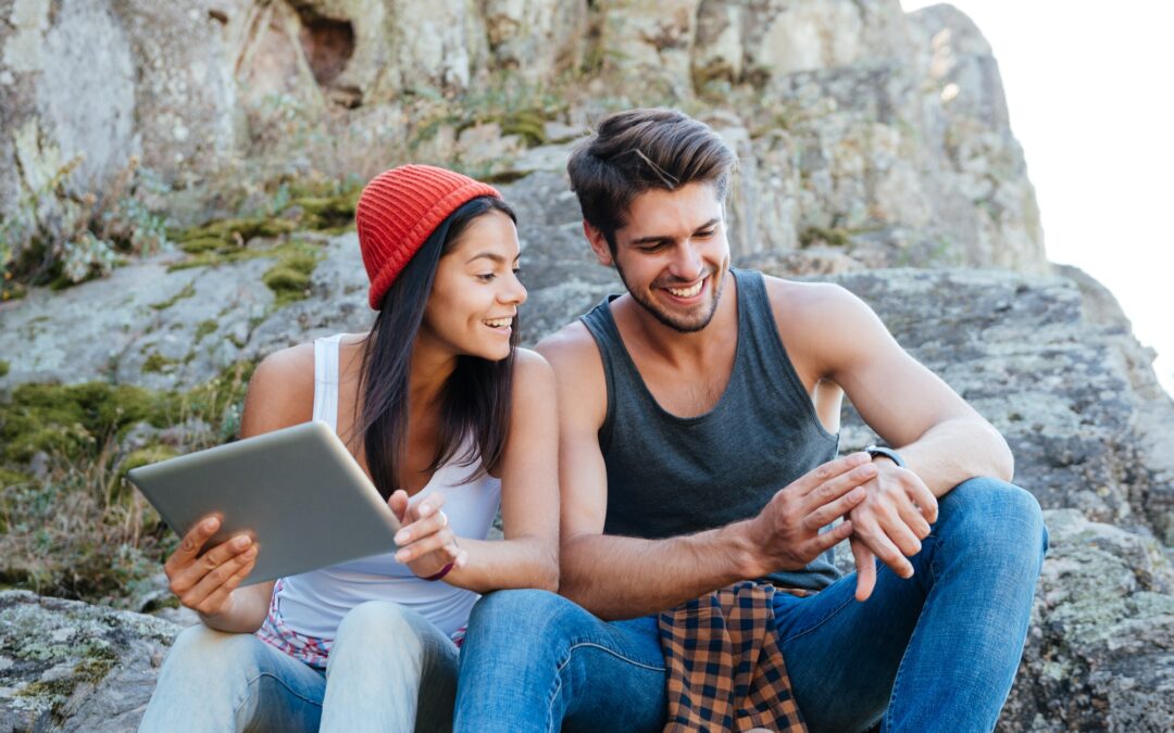 Happy young couple sitting together with tablet and using smartwatch